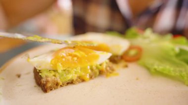 Avokado tostunun üzeri yumurta kesimiyle kaplıyken yanında yeşil ve domates garnitürlü yumurta sarısı, ev yapımı sağlıklı brunch konsepti.