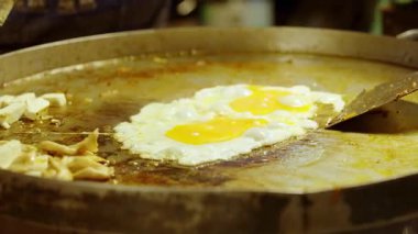 Tofu ve diğer malzemelerle büyük sıcak tavada kızaran yumurtaları yakın. Tayland sokak pazarında Pad Thai pişirirken.