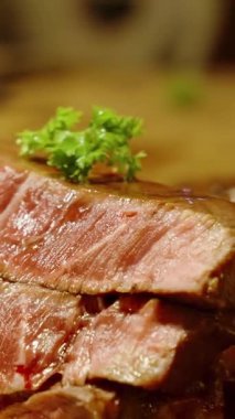 Dikey video. Sıcak mutfak ışıklarıyla süslenmiş taze maydanozla dolu orta pişmiş lezzetli biftek dilimlerini kapatın. Gurme Et Konsepti.