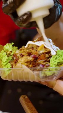 Dikey video. Tedarikçinin kapısına git ve tako üzerine mayonez sosu ekle. Plastik tepside et ve marul karışımı. Yemek standında müşterilere servis yaparken.