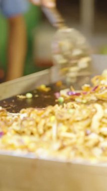 Dikey video. Siyah eldiven giyip kapak yap. Kızarmış sebzeleri karıştır, kıvırcık salatayı plastik tepsiye koy. Gece pazarında ızgara yap.