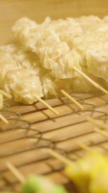 Dikey video. Çeşitli şiş köftelere ve buharı yükselen bambu buharlı bir buharlı buharlı Çin böreğine, geleneksel Asya sokak yemeği kavramına yakın durun.