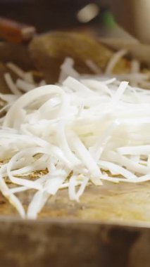 Dikey video. Sokak satıcısının, canlı pazar atmosferinde yumurtalarla Pad Thai pişirirken büyük sıcak tavada soslu beyaz pirinç şehriyesi karıştırması, Sokak Gıda Konsepti.