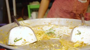 Sokak satıcısını hemen kapatın. Tayland pazarında Pad Thai pişirirken tofu ve fasulye filizlerini büyük sıcak tavada spatulayla karıştırın. Sokak Gıda Konsepti.