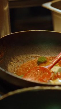 Dikey video. Makarnanın sıcak tavaya domatesli ve soslu bir şekilde gaz sobasında, düşük açılı, sokak aşçılığı kavramında mavi ateşin üzerine eklenmesi.