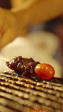 Dikey video. Elle ızgara et şişi ve domatesle metal sos kabının yanındaki ızgaranın üzerine sığ bir alan derinliği, sokak yemekleri konsepti.