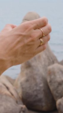 Dikey video. Yüzük Giyen Kadın Yüzükleri Samui Adası 'nda Deniz kenarındaki Iconic Hin Ta Hin Yai Kaya oluşumlarını işaret ediyor.