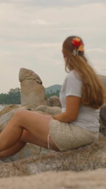 Dikey video. Kayalıklarda Oturan Kadın Samui Adası 'nda Deniz Tarafından Ünlü Hin Ta Hin Yai Kaya oluşumlarına Bakıyor.