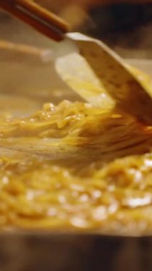 Dikey video. Yavaş Çekim Pad Tayland Eriştesi. Tayland pazarında Spatula in Large Hot Pan, yakın açı, Sokak Gıda Konsepti.