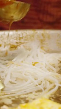 Dikey video. Angle Slow Motion Şefi Sos ve Çiğ Pad Tayland Eriştesini Büyük Sıcak Tavada Metal Utensillerle Karıştırıyor, Sokak Gıda Konsepti