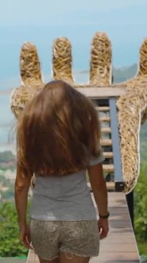 Dikey video. Büyük tahta el üzerinde yürüyen kadın deniz ve yeşil tepeler üzerinde güneşli havada, geniş açı manzaralı, çakışan taş Koh Samui konsepti seyahat ilhamı