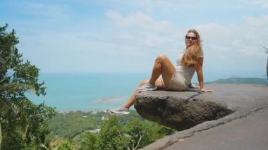 Üst üste binen taşın üzerinde oturan genç kadın geniş okyanus manzaralı ağaçlarla çevrili kenar açılı geniş açılı Samui Doğa Macerası