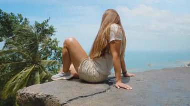 Arka planda Ağaçlar ve Okyanusla Uçurumun kenarında oturan Genç Kadın Üst üste Taş Samui, Açık Hava Gevşeme Konsepti