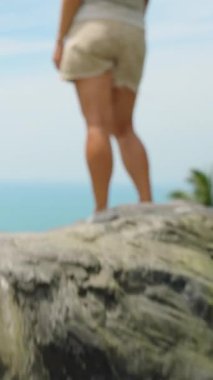 Dikey video. Zorlu Taş Basamakları 'na tırmanan Üst Düzlükte Duran Bir Kadın Ocean View from Low Angle at Sublap Stone Samui, Macera Yolculuğu Konsepti