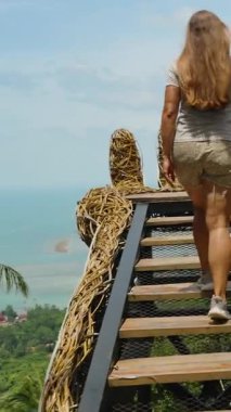 Dikey video. Ocean ve Hills manzaralı dev el yapısının Tahta Merdivenlerden Yukarı Yürüyen Bir Kadın Takibi Üst üste binen taştan Samui, Macera Yolculuğu Konsepti