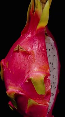 Dikey video. Tüm Pembe Ejderha Meyvesi, Siyah Tohumlarla Siyah Arkaplan, Egzotik Tropikal Meyve Konseptine Karşı Siyah Tohumları Gösterirken Döngüde Dönüyor