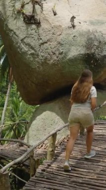 Dikey video. Dar Tahta Köprüde Yürüyen Kadın Arkaplanda Okyanus manzaralı Büyük Dengeli Kaya 'ya Üst üste Taş Samui' de Yüksek Açı, Keşif Macerası Konsepti