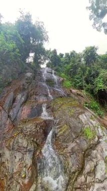 Dikey video. Çevrelerinde Koh Samui 'deki Yeşil Orman ile çevrili Şelaleden Kamera Şelaleden Kayalara Sıçrayan Kayaların Dinamik Görünümünü Kapat Geniş Açı Doğa Eyleminde Yakala