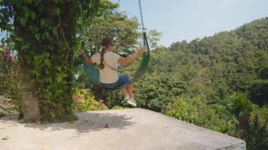 Güneşli bir günde Orman Ağaçları ve Tropikal Bitkilerle çevrili Beton Platformun Üzerinde Sallanan Kadın, Açık Hava Özgürlük Konsepti