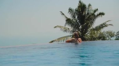 Uzakta Palmiye ağacı ve Okyanus ile Havuz kenarına yaslanan Kadın Görünümü, Huzurlu Kaçış Konsepti