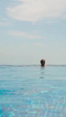 Dikey video. Uçsuz bucaksız havuzun kenarında dinlenen Mavi Gökyüzü ve Sakin Su ile Ufuk 'a Bakan Kadın, Huzur Konsepti