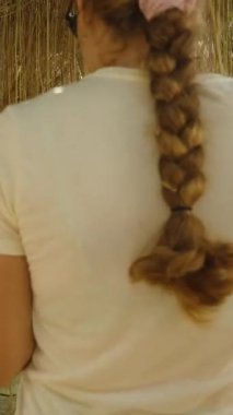 Dikey video. Güneş ışığı ve ağaçlarla çevrili Parlak Tropikal Bahçede Asılı Kökler Arasında Yürüyen Uzun Örgülü Saçlı Kadın, Doğa Keşfi