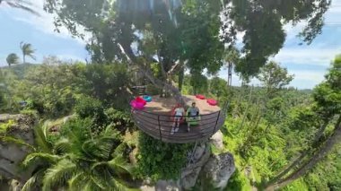 Erkek ve Kadın Yükseltilmiş Güvertenin Kıyısında Oturuyor Ağaçlarla çevrili Renkli Fasulye Torbaları ve Dağ Ormanı Manzarası, Geniş Açı, Tropikal İnziva Konsepti