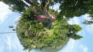 Küçük Gezegen Görünümü Orman ve Gökyüzü, Küçük Gezegen Efekti, Egzotik Seyahat Konsepti ile Ağaçların Arasında Asılı Güvertede Oturan Erkek ve Kadın