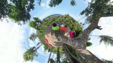 Palmiye Ağaçları ve Eğri Gökyüzü, Küçük Gezegen Efekti, Dijital Gevşeme Konsepti ile çevrili Minik Gezegen Görünümü 'ndeki Ağaç Güvertesinde Telefonlarla Oturan Çift