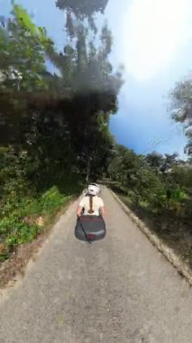 Dikey video. Scooter 'da Erkek Sürücünün Arkasında Oturan 360 derecelik Gölgeli Ormanda Tepeye Sürülen Kadın Macera Yolculuğu Konsepti