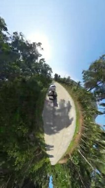 Dikey video. 360 Derece Minik Gezegen Görünümü, Macera Yolculuğu Konsepti 'nde Diri Ağaçlarla çevrili Scooter' la Arkadaki Kadın