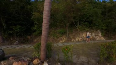 Bereketli Yeşillik ve Okyanus 'tan Palmiye Ağaçlarıyla Yürüyen Kadın, FPV İHA Arka İzleme Çekimi, Rahat Seyahat Konsepti