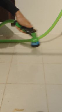 Dikey video. Beyaz Duvar 'ın yakınındaki Döşeme Balkonunda Çıplak Ayaklı Sprey Suyu Temizleme Sahnesinde Yeşil Hortum