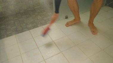Çıplak ayakla Beyaz Banyo Döşemesini Kırmızı ve Mavi Temizlik Fırçasıyla Temizleyen Kişi