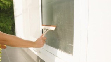 Parlak güneş ışığında cam penceredeki sabunlu suyu temizlemek için beyaz cam sileceği kullanmak, açık hava temizlik kavramı.
