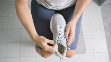 Oturan ve Bağlayan Gri Atletik Ayakkabılı Mavi Tırnak Cilalı Kadın Yukarıdan Bakış Açısı