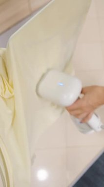 Dikey video. Sarı Tişörtte Buharlı Kadın Kullanımı Askıda, Üst Açı, Çamaşır Bakımı Konsepti