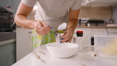 Mutfak tezgahında kaşıkla konserve bezelyeleri kepçeleyen kadın, yakın çekim açısı, ev yemeği kavramı.