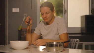 Mutfak Masası, Orta Açı, Ev Yapımı Yemek Konsepti 'nde otururken kaşıkla Metal Kap Yiyen Kadın