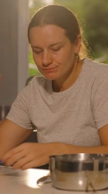 Dikey video. Mutfak Masası, Orta Açı, Ev Yapımı Yemek Konsepti 'nde otururken kaşıkla Metal Kap Yiyen Kadın