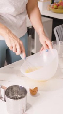 Dikey video. White Bowl 'da Yenilmiş Yumurta' yı Mutfak tezgahında Un, Yan Açı, Pasta Hazırlama Konseptiyle Karıştıran Kadın