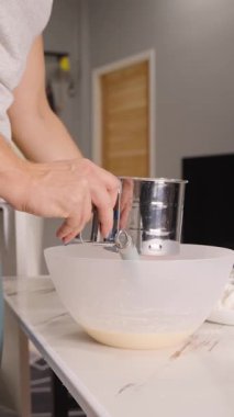 Dikey video. Metal Sifter, Yan Açı, Hamur Yapımı Kavramını Tutarken Beyaz Kasede Yumurta Karıştıran Kadın Unu