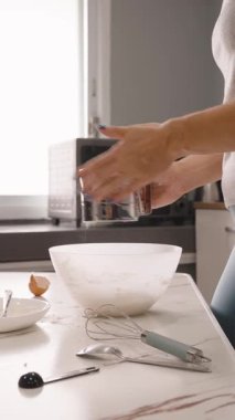 Dikey video. Mutfak tezgahında Beyaz Kase 'ye Un yerleştiren Kadın Çevrede Fırın Aletleri, Yan Açı, Pasta Hazırlama Konsepti