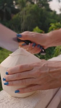 Dikey video. Açık havada hindistan cevizi doğrama ve hindistan cevizi suyu sıçratma, egzotik içecekler