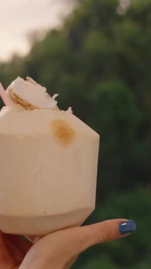 Dikey video. Yeşil Tropikal Arkaplana Karşı Kadın Eli Altında tutulan Hindistan cevizi, Egzotik İçeceğe Yönelik