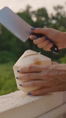 Dikey video. Büyük Bıçaklı Taze Hindistan cevizini Yavaş Çekimde Kesen Kadın Meyve Suyu Sıçratırken, Egzotik Serinletici Kavram