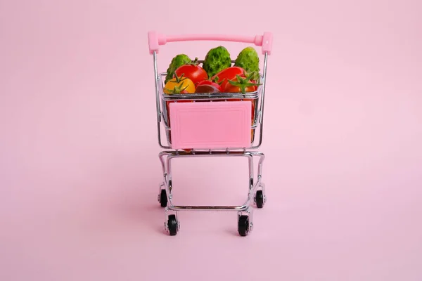 Rózsaszín Bevásárlókocsi Tele Paradicsommal Uborkával Rózsaszín Alapon — Stock Fotó