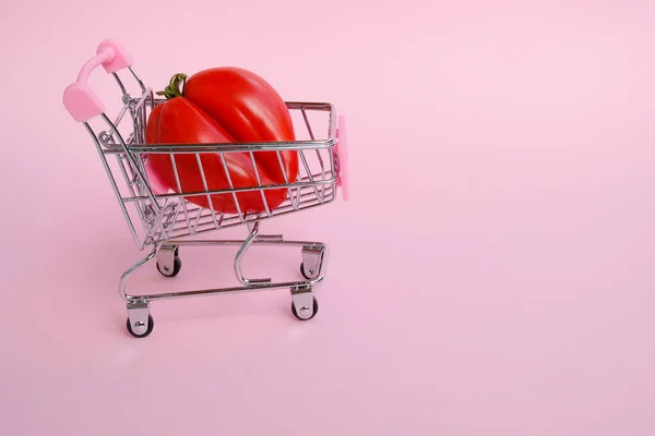 Kleine Kruidenierswinkelwagentje Met Grote Ongewone Tomaat Roze Achtergrond — Stockfoto