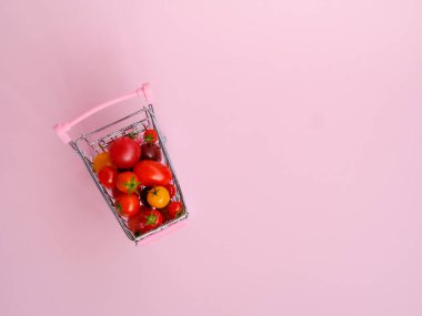 Pembe arka planda domateslerle dolu pembe market arabası
