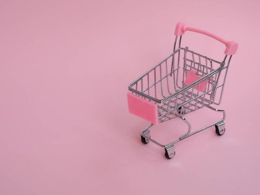 Pembe arka planda büyük sıra dışı salatalıkları olan küçük market arabası.